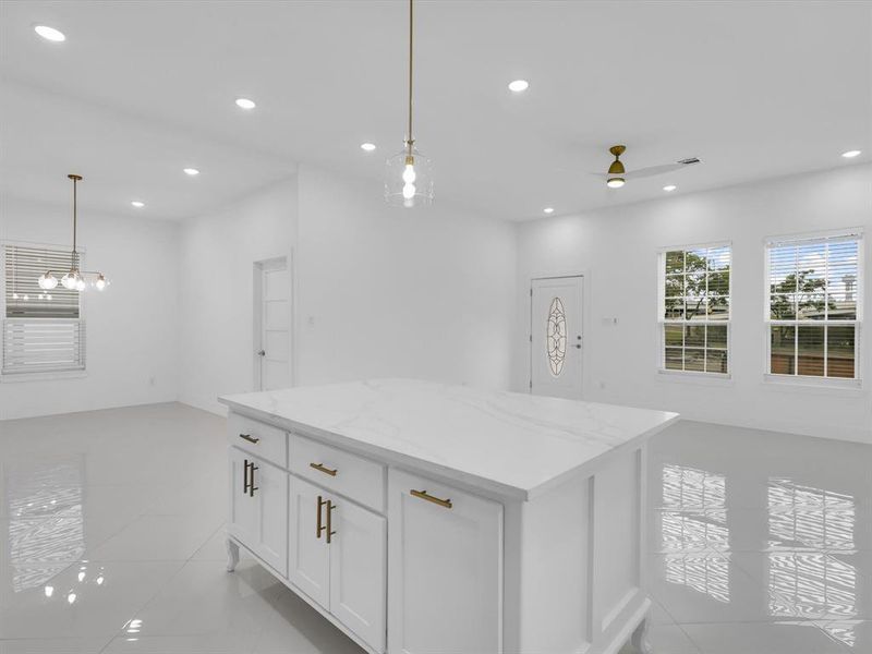 Kitchen with light stone countertops, light tile patterned floors, decorative light fixtures, a kitchen island, and white cabinets