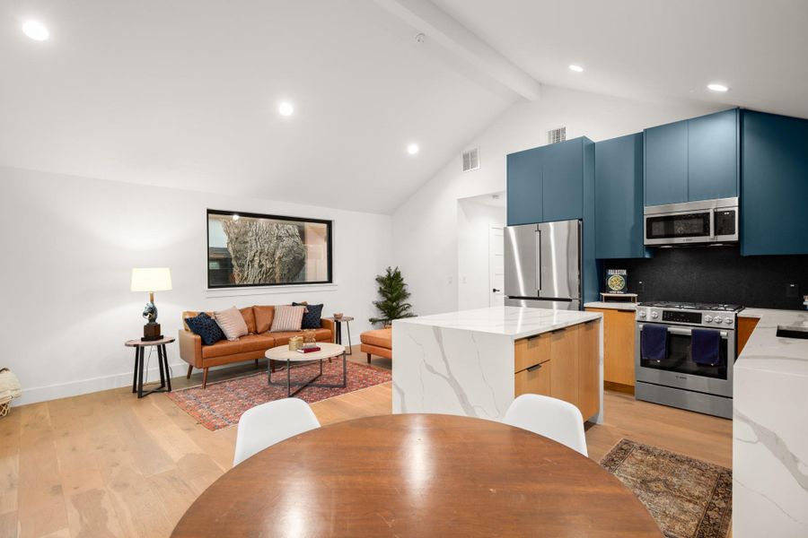 Kitchen featuring light stone counters, stainless steel appliances, light wood finished floors, beamed ceiling, and open floor plan