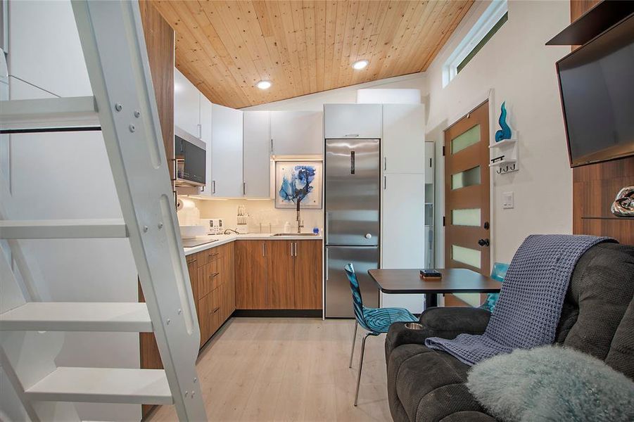 Kitchen featuring white cabinetry, brown cabinets, appliances with stainless steel finishes, light countertops, and vaulted ceiling Kitchen featuring white cabinetry, brown cabinets, appliances with stainless steel finishes, light countertops, and vaulted ceiling
