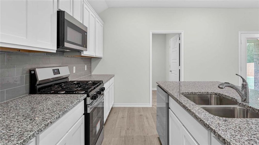 Kitchen featuring white cabinetry, gray subway tile backsplash, stainless steel gas range, stainless steel over-the-range microwave, and light-colored wood-finish flooring