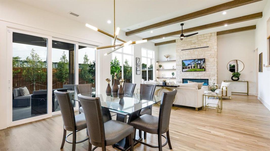 Dining area with beamed ceiling, a stone fireplace, light wood-type flooring, and ceiling fan