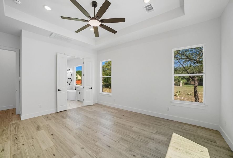 Unfurnished bedroom with a tray ceiling, light wood-type flooring, recessed lighting, ceiling fan, and ensuite bathroom Unfurnished bedroom with a tray ceiling, light wood-type flooring, recessed lighting, ceiling fan, and ensuite bathroom