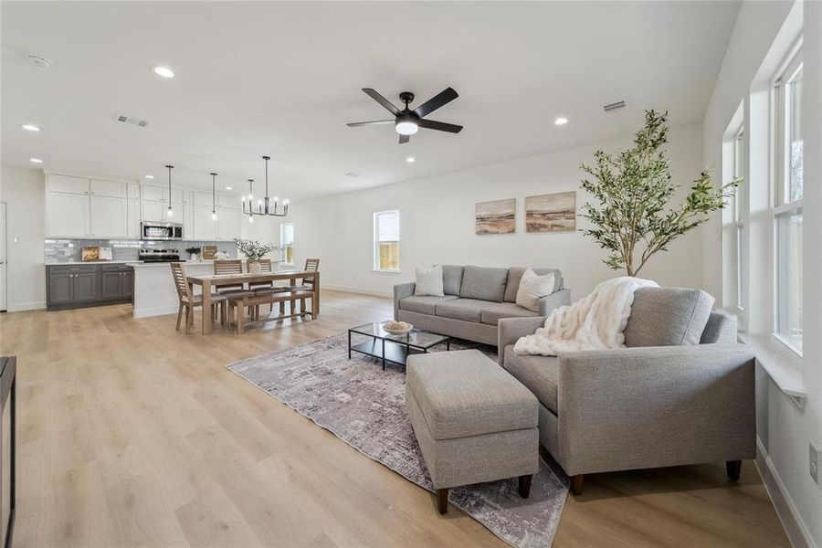 Living room with ceiling fan with notable chandelier and light wood-type flooring