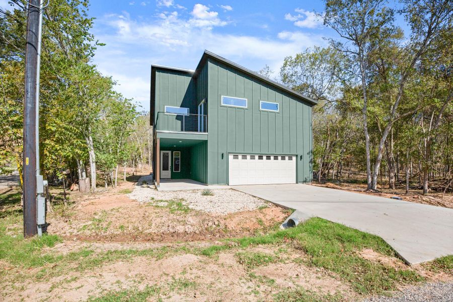 View of front facade with board and batten siding, a patio area, an attached garage, driveway, and a balcony