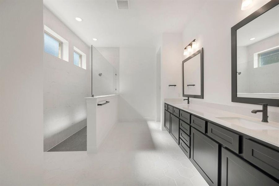 Contemporary bathroom featuring a spacious walk-in shower with glass enclosure, dual vanity with undermount sinks, dark cabinetry, and hexagonal floor tiling Contemporary bathroom featuring a spacious walk-in shower with glass enclosure, dual vanity with undermount sinks, dark cabinetry, and hexagonal floor tiling