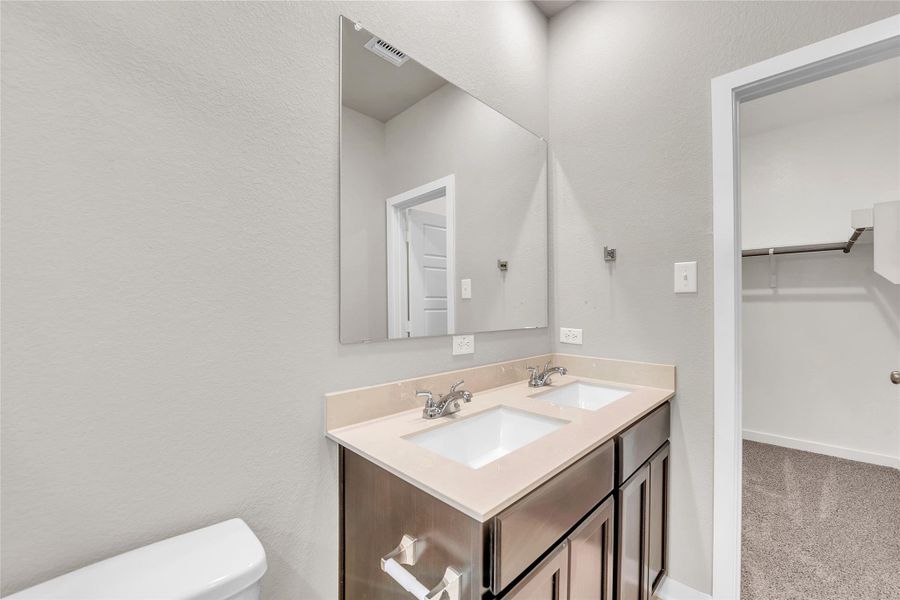 Bathroom featuring double vanity, a walk in closet, a textured wall, and light colored carpet