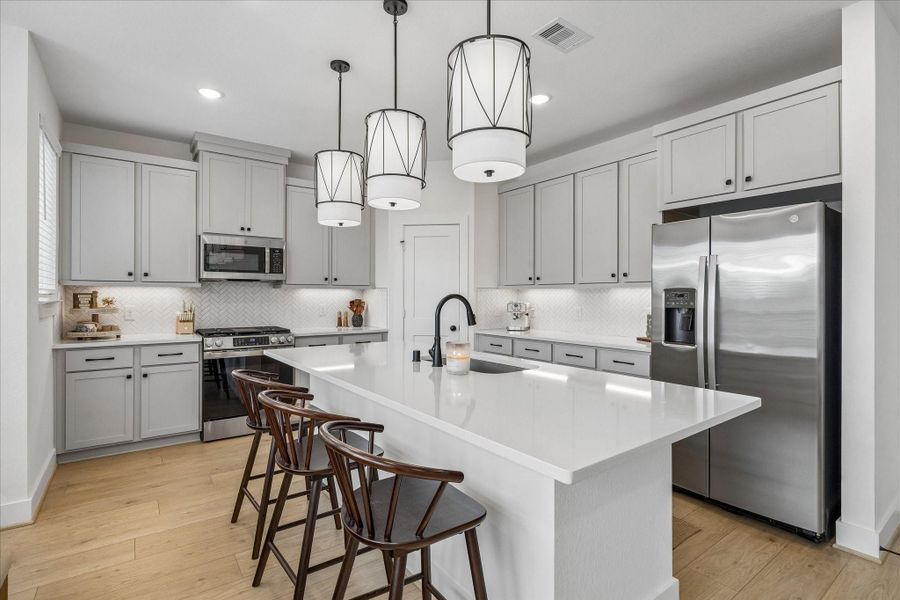 The well-appointed kitchen features an oversized quartz island, abundant cabinetry, a walk-in pantry, stainless steel appliances, and stylish pendant lighting.