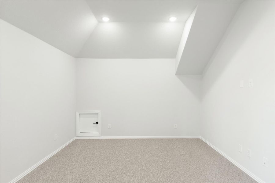 Empty room with vaulted ceiling, recessed lighting, carpet flooring, and small access door on white wall