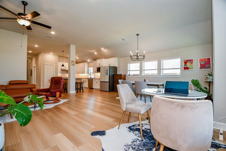 This inviting open-concept living space features modern hardwood floors, a cozy seating area, and a dining nook. The kitchen is equipped with contemporary appliances and ample cabinetry, while large windows provide plenty of natural light. A ceiling fan and tasteful lighting fixtures add comfort and style.