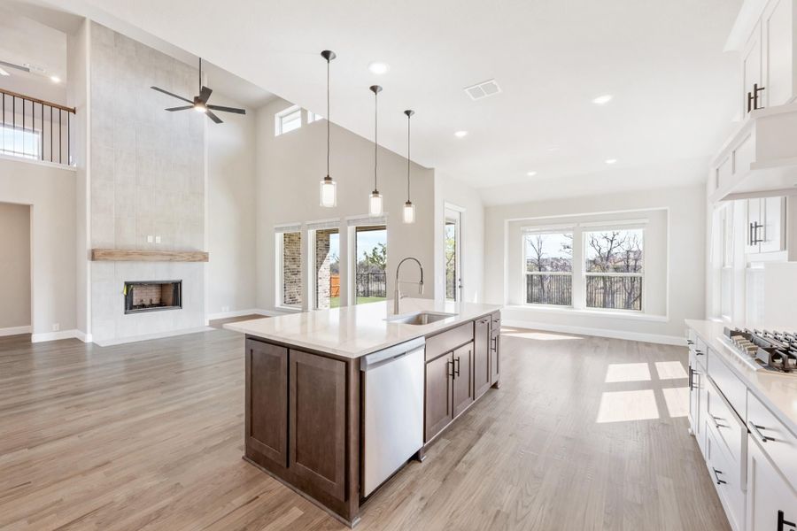 Open-concept kitchen with dark wood island, pendant lights, and fireplace in adjoining living area with vaulted ceiling