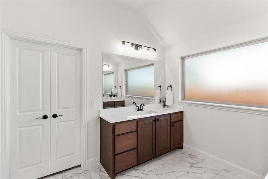 Bathroom featuring vanity, light marble finish flooring, and lofted ceiling