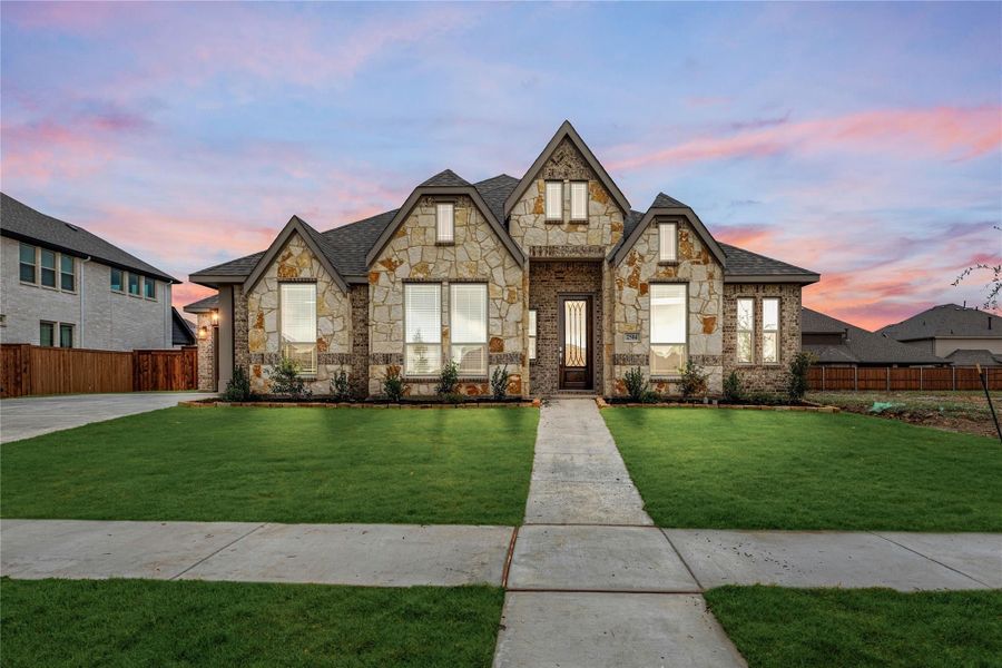 Single-story home with stone and brick exterior, peaked roofline, and manicured front lawn with concrete walkway