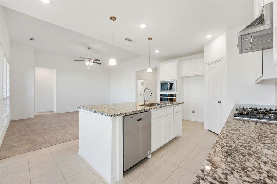 Kitchen with light carpet, white cabinets, an island with sink, and stainless steel appliances