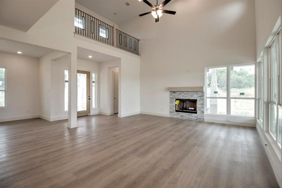 Unfurnished living room featuring a fireplace, a towering ceiling, light wood-style flooring, ceiling fan, and recessed lighting Unfurnished living room featuring a fireplace, a towering ceiling, light wood-style flooring, ceiling fan, and recessed lighting