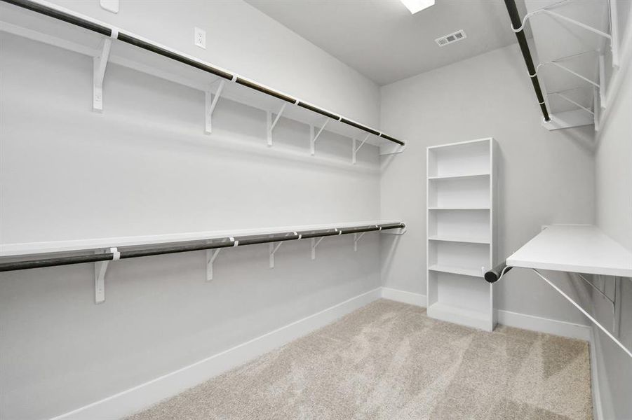 Experience luxury in this spacious walk-in closet with high ceilings and plush carpet. Warm paint tones, built-in shelving, and dark finishes create a contemporary and functional retreat