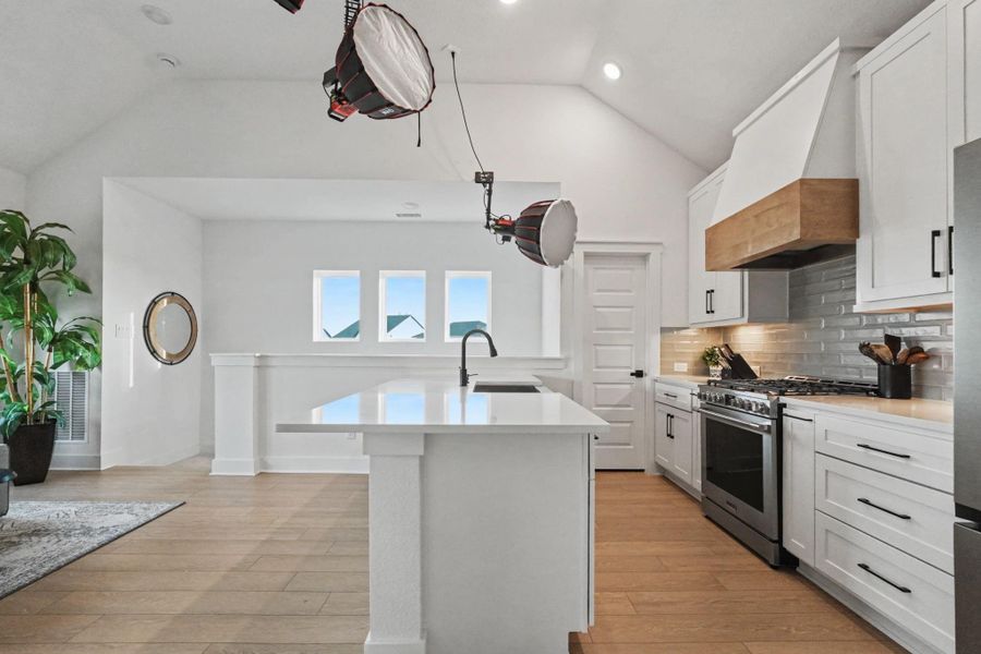 Bright and inviting kitchen with a spacious island, quartz countertops, stainless appliances, and a custom vent hood. Open sightlines and vaulted ceilings enhance the airy, modern feel of this beautifully designed space.