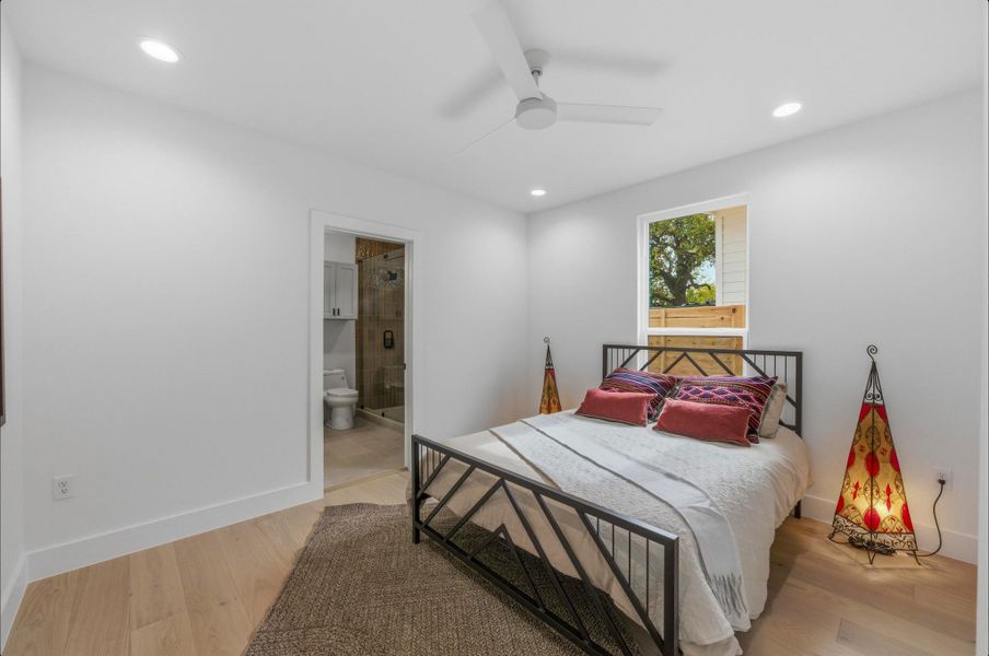 Bedroom with light wood finished floors, ceiling fan, ensuite bathroom, and recessed lighting