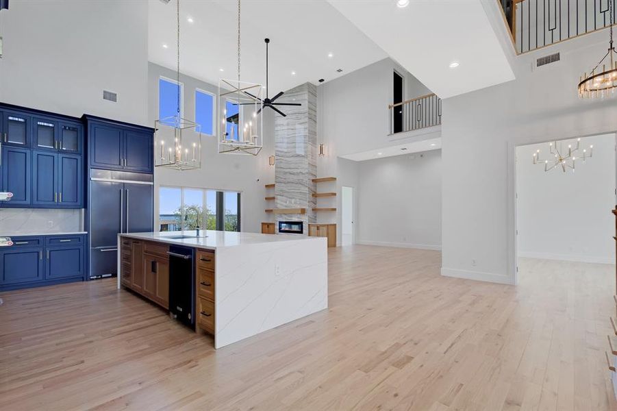 Spacious open-concept living area featuring high ceilings, wood-finish flooring, and a floor-to-ceiling fireplace with integrated shelving