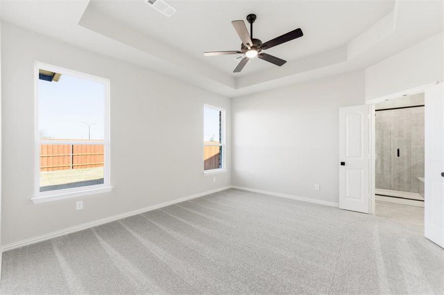 Unfurnished room with a raised ceiling, light carpet, and ceiling fan