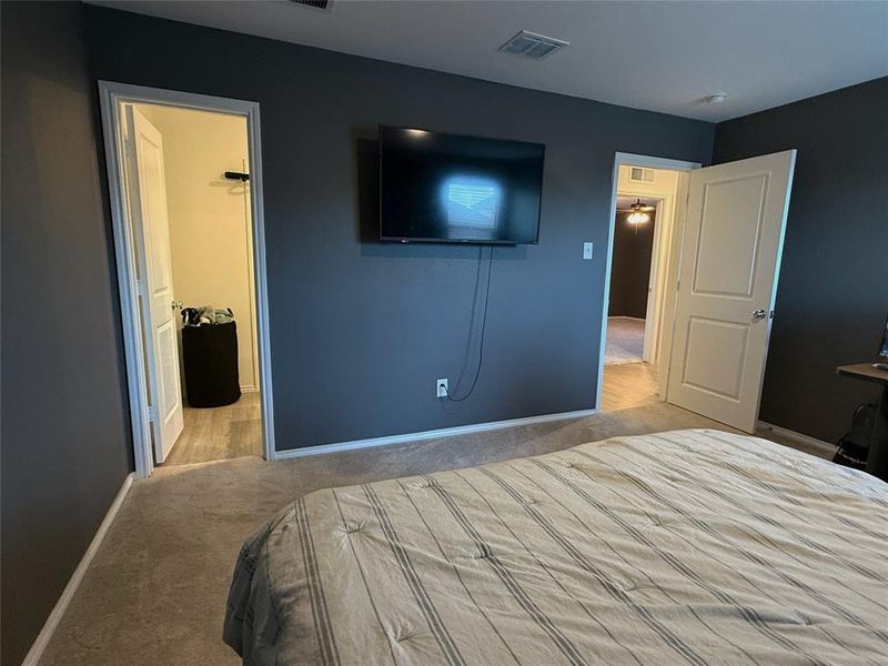 Carpeted bedroom featuring a wall-mounted display, dark accent wall, and white trim Carpeted bedroom featuring a wall-mounted display, dark accent wall, and white trim
