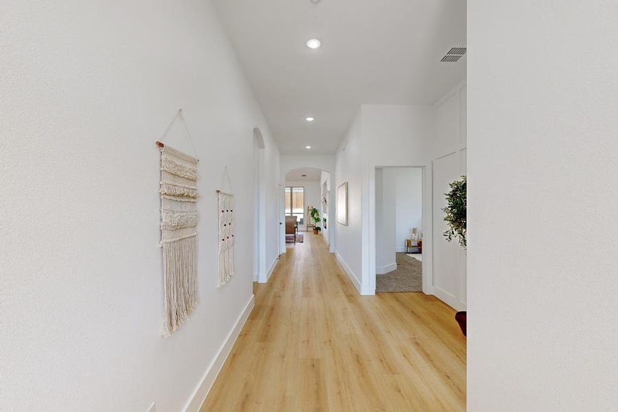 Corridor with arched walkways, light wood-style flooring, and recessed lighting