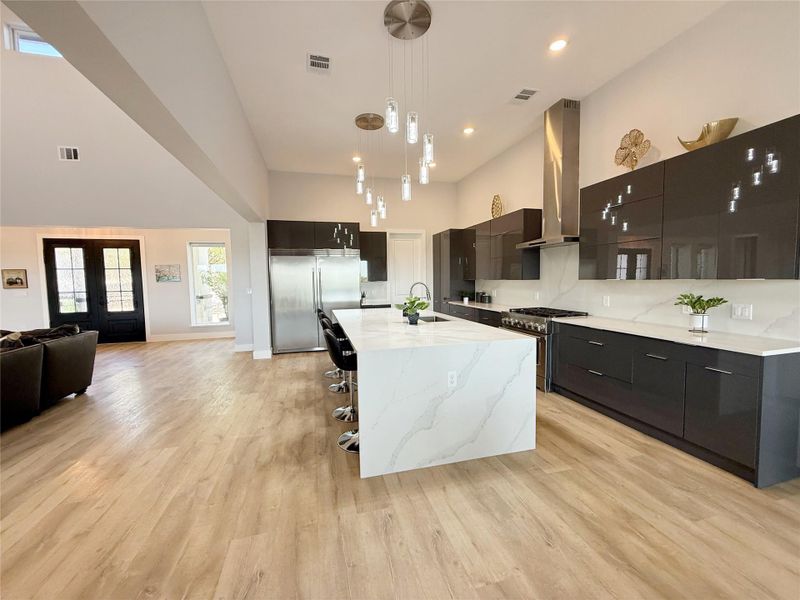 Kitchen with modern cabinets, dark cabinetry, high quality appliances, hanging light fixtures, and open floor plan