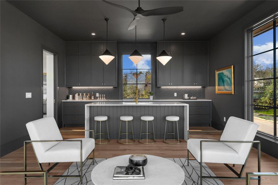 Kitchen featuring gray cabinets, wood finished floors, light countertops, a center island with sink, and backsplash Kitchen featuring gray cabinets, wood finished floors, light countertops, a center island with sink, and backsplash