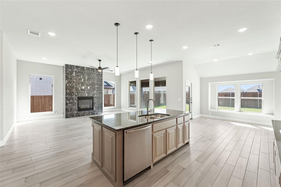 Open-concept kitchen with large island, dark countertops, and pendant lights, open to living area with stone fireplace Open-concept kitchen with large island, dark countertops, and pendant lights, open to living area with stone fireplace