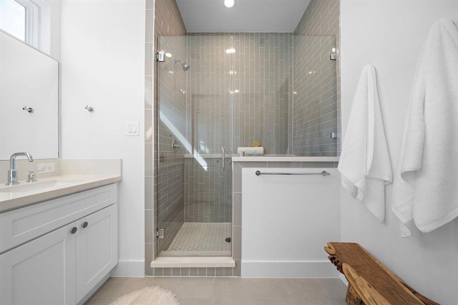 Primary bathroom featuring a large walk-in shower with floor to ceiling tile and towel hooks!