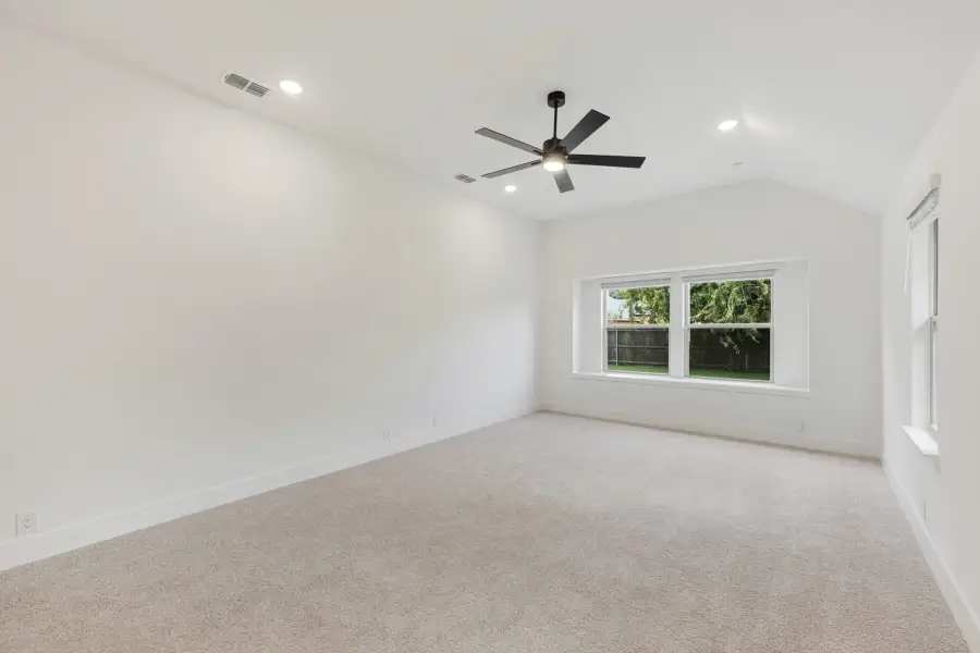 Empty bedroom with vaulted ceiling, black ceiling fan, carpet flooring, and a backyard-facing window