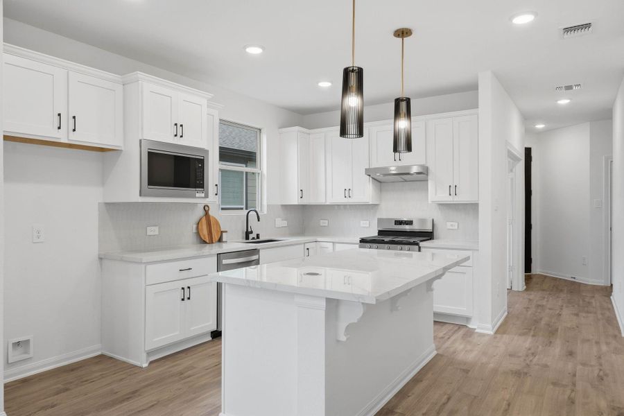 This modern kitchen balances style and function with white cabinetry, stainless steel appliances, pendant lighting, and a bright, open layout.