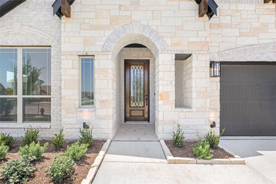 Stone home entrance with arched doorway, wood and glass front door, and attached garage