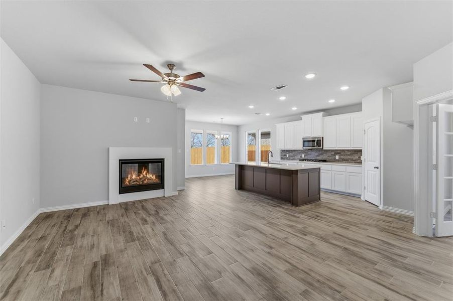 Kitchen featuring open floor plan, a glass covered fireplace, ceiling fan, a center island with sink, and light wood-style floors