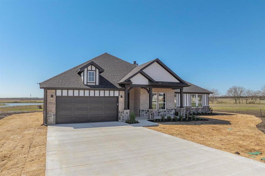 View of front of property featuring brick siding, a shingled roof, a porch, a garage, and driveway