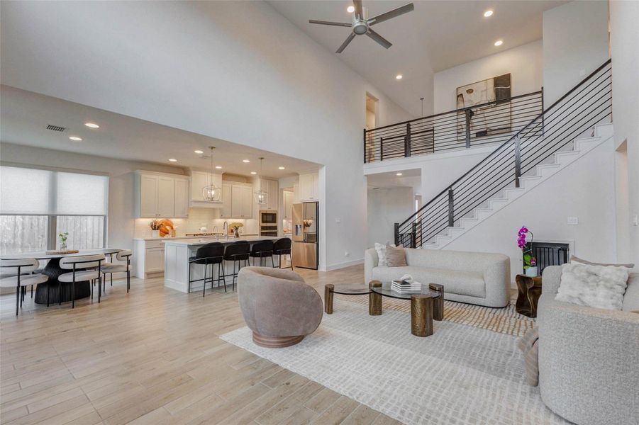 Open-concept living area with high ceilings, featuring a modern kitchen with an island and bar seating, a cozy dining area, and a stylish living room. A sleek staircase leads to the upper level, enhancing the contemporary design. Open-concept living area with high ceilings, featuring a modern kitchen with an island and bar seating, a cozy dining area, and a stylish living room. A sleek staircase leads to the upper level, enhancing the contemporary design.