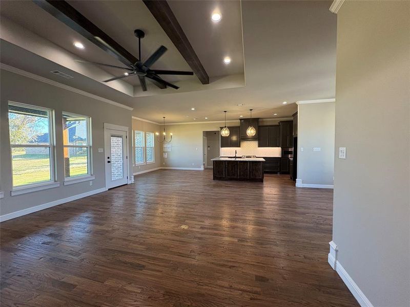 Unfurnished living room featuring beam ceiling, crown molding, dark wood-style flooring, a ceiling fan, and a chandelier