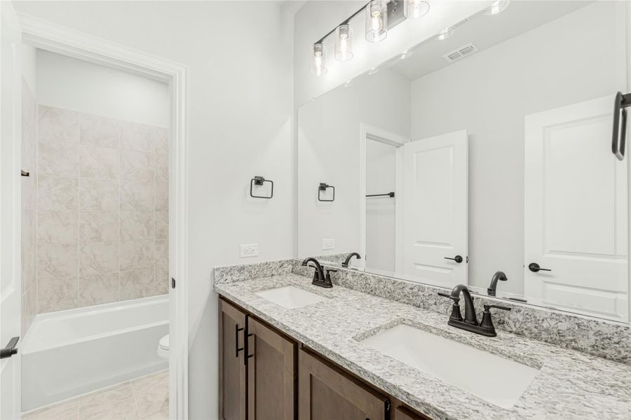 Bathroom with double sink vanity, granite countertop, dark wood cabinets, and tiled tub-shower combo Bathroom with double sink vanity, granite countertop, dark wood cabinets, and tiled tub-shower combo