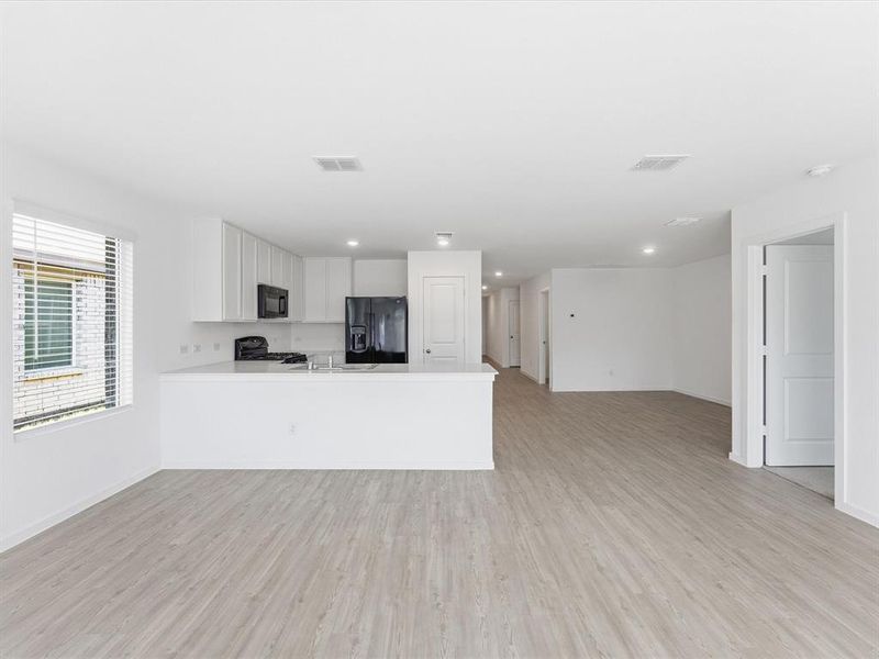 Open-concept kitchen and living area featuring light wood-finish flooring, white cabinetry, a large kitchen island, and black appliances
