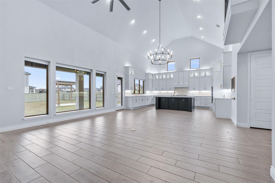 Unfurnished living room featuring high vaulted ceiling, a chandelier, wood finish floors, ceiling fan, and recessed lighting