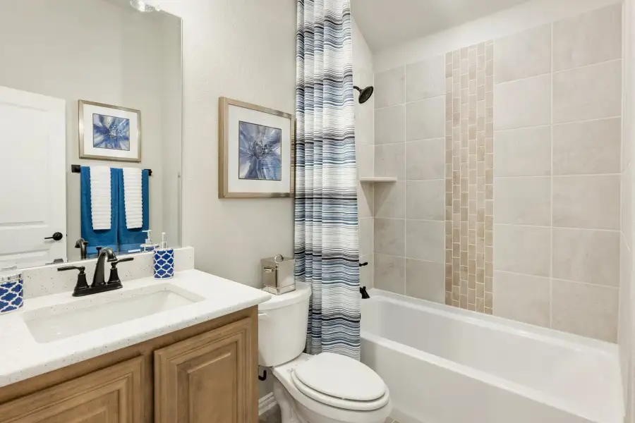 Bathroom with wood vanity, white countertop, toilet, and tiled tub-shower combo with striped curtain