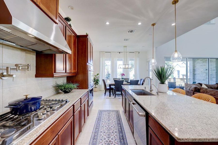 Kitchen with under cabinet range hood, stainless steel appliances, light stone counters, recessed lighting, and decorative backsplash
