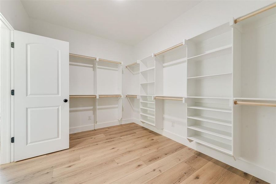 Walk-in closet featuring extensive built-in shelving, multiple hanging rods, dedicated shoe storage, and light wood-finish flooring