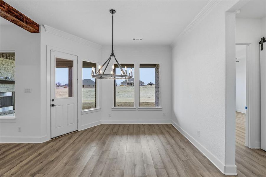 Unfurnished dining area featuring a chandelier, light wood-type flooring, a barn door, and ornamental molding