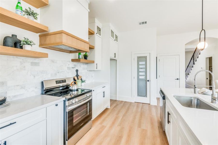 Kitchen with premium range hood, hanging light fixtures, stainless steel appliances, and white cabinets