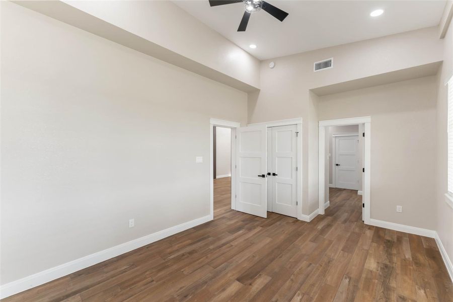 This spacious interior features high ceilings, tile wood-style flooring, and taupe walls. It includes a ceiling fan and recessed lighting, providing a modern and airy feel. Multiple doors lead to adjacent rooms, enhancing connectivity throughout the space.