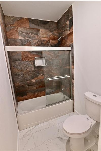 Bathroom with tile patterned floors, bath / shower combo with glass door, and toilet