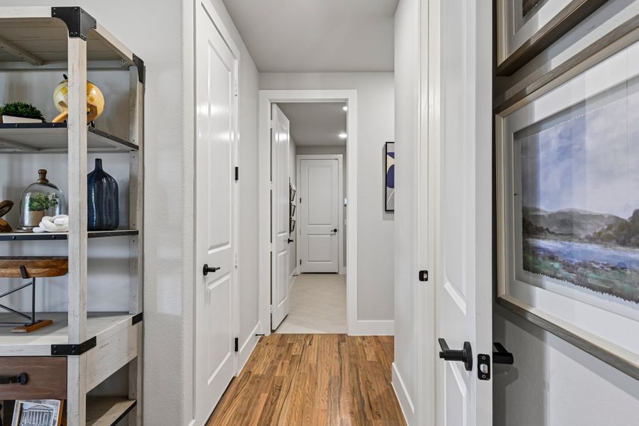 Hallway with white walls, hardwood floors, white panel doors, and a decorative open shelving unit on the left.