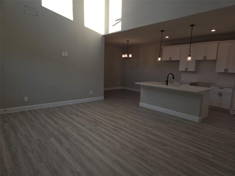 Kitchen featuring a towering ceiling, wood-type flooring, a center island with sink, decorative light fixtures, and white cabinetry