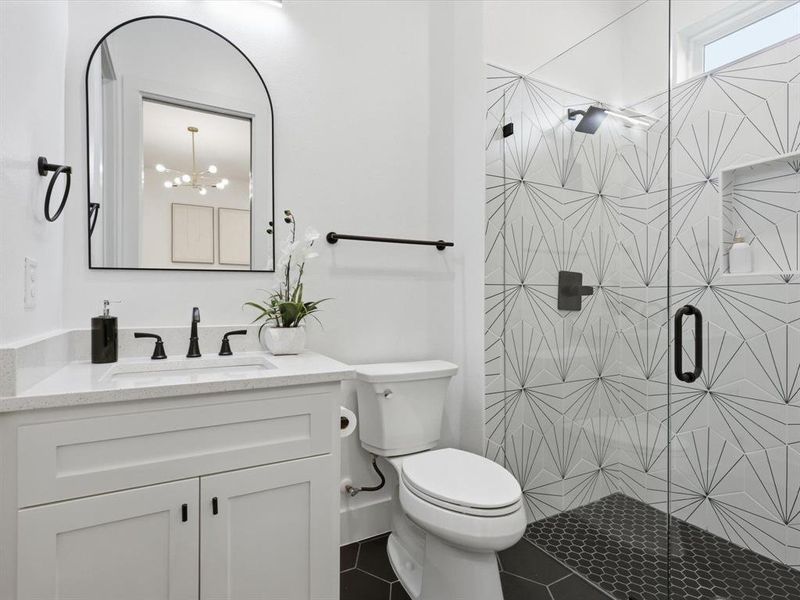 Ensuite bathroom to a secondary bedroom, modern bathroom featuring a glass-enclosed shower with geometric tile, white vanity with quartz countertop, and matte black fixtures