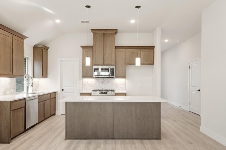Kitchen with center island, brown cabinets, stainless steel appliances, pendant lights, and light wood floors
